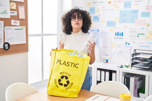 事務所でプラスチックボトルでリサイクルバッグを保持若い中東の女性は懐疑的で緊張し 問題のために動揺を眉をひそめて 否定的な人 — ストック写真