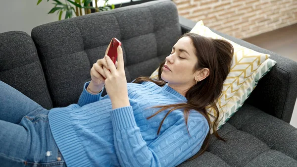 若いです白人女性使用スマートフォン嘘上のソファ ホーム — ストック写真