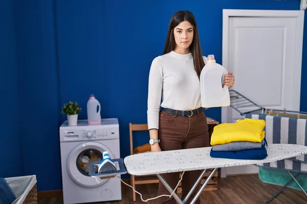 Young brunette woman with folded laundry after ironing thinking attitude and sober expression looking self confident