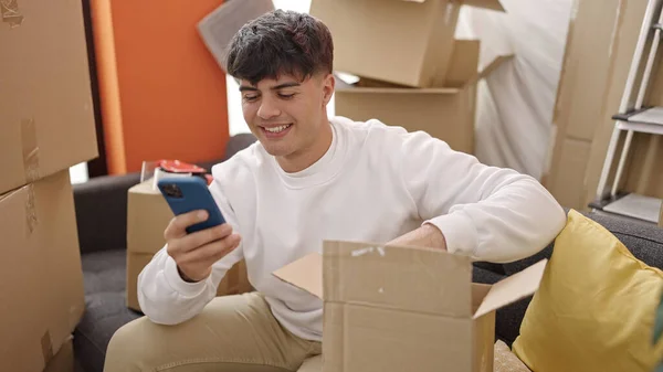 Młody Hiszpan Rozpakowuje Kartonowe Pudełko Pomocą Smartfona Nowym Domu — Zdjęcie stockowe
