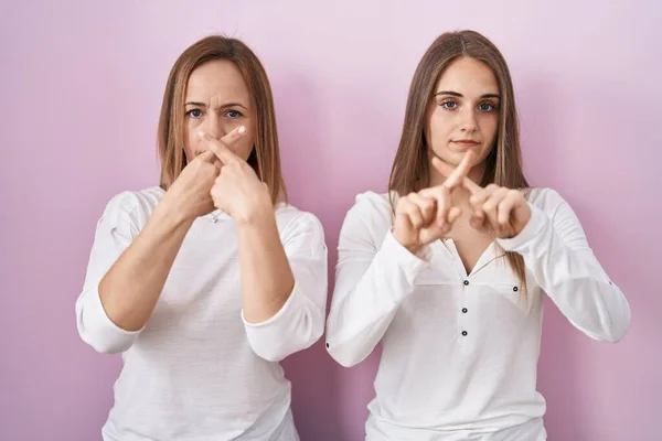 中年母亲和年幼的女儿站在粉红的背景下 用手指表示拒绝 做阴性手势 — 图库照片