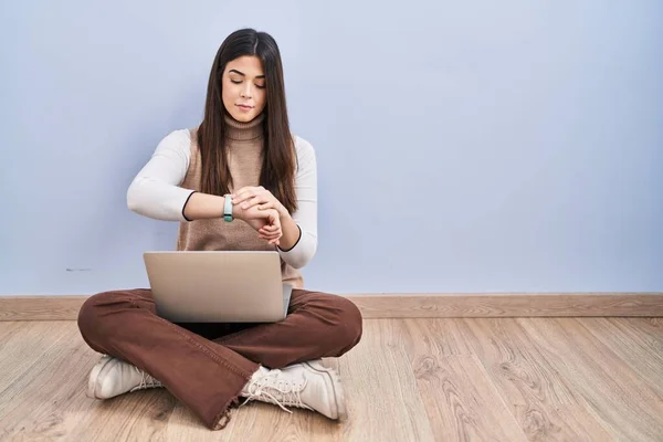 使用电脑笔记本电脑工作的年轻黑发女人坐在地板上检查腕表上的时间 放松而自信 — 图库照片