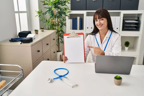 Young Brunette Doctor Woman Holding Clipboard Smiling Happy Pointing Hand — Stock Photo, Image