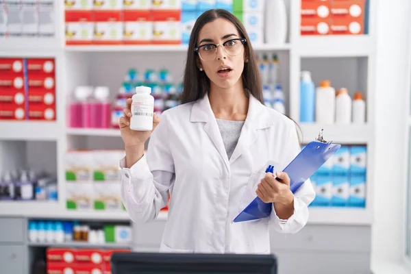 Jovem Morena Que Trabalha Farmácia Farmácia Segurando Pílulas Rosto Choque — Fotografia de Stock