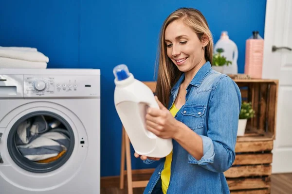 Young Blonde Woman Washing Clothes Holding Detergent Bottle Laundry Room — Stock Photo, Image
