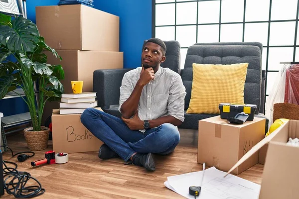 アフリカ系アメリカ人の男性は 集中的な表現について考えて手で新しい家の床に座っている 思慮深い顔で笑顔 疑わしい概念 — ストック写真