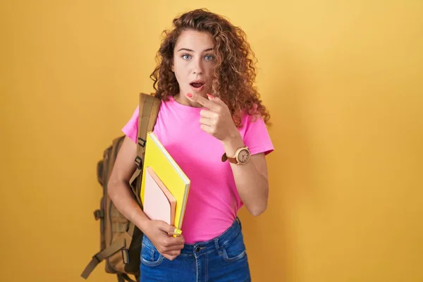 Young Caucasian Woman Wearing Student Backpack Holding Books Surprised Pointing — Stock Photo, Image