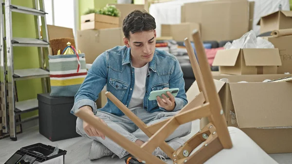 Young Hispanic Man Repairing Chair Using Screwdriver Smartphone New Home — Stock Photo, Image