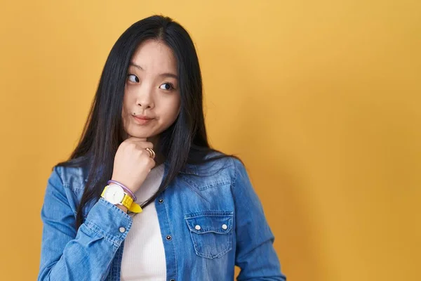 Młoda Azjatka Stojąca Nad Żółtym Tłem Ręką Podbródku Myśląca Pytaniu — Zdjęcie stockowe
