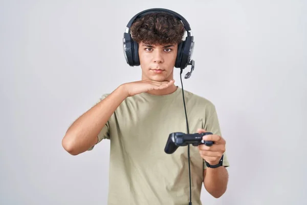 stock image Hispanic teenager playing video game holding controller cutting throat with hand as knife, threaten aggression with furious violence 
