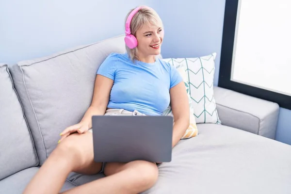 Young Blonde Woman Using Laptop Headphones Lying Sofa Home — ストック写真