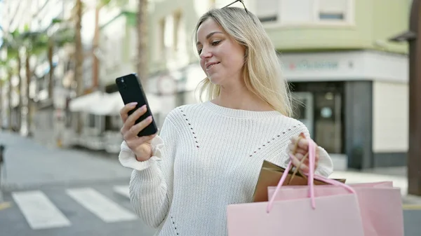 Młoda Blondynka Idzie Zakupy Trzymając Torby Pomocą Smartfona Ulicy — Zdjęcie stockowe