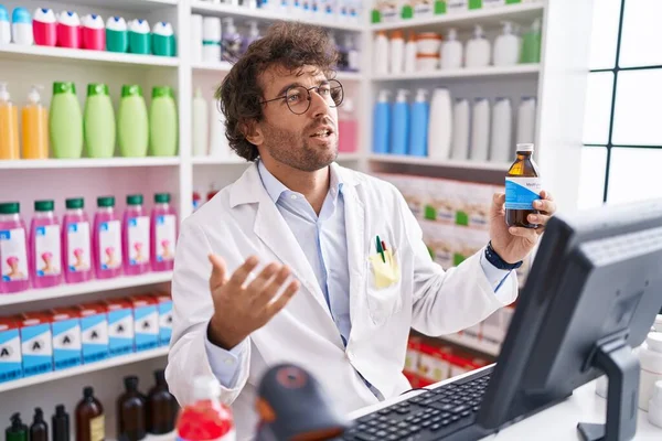 Young Hispanic Man Pharmacist Holding Medication Bottle Speaking Pharmacy — Foto Stock