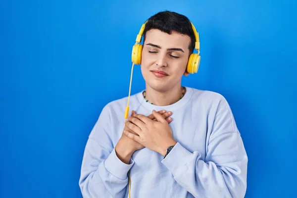 ヘッドフォンを使用して音楽を聴いている非バイナリ人は 目を閉じて胸に手を笑顔と顔に感謝のジェスチャーを使用しています 健康の概念 — ストック写真