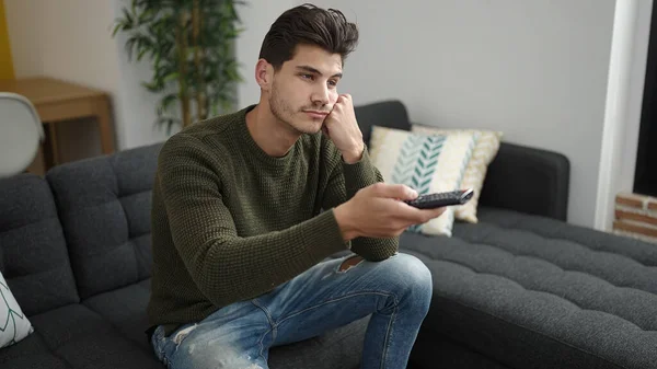 Young Hispanic Man Watching Sitting Sofa Boring Expression Home — Stok fotoğraf
