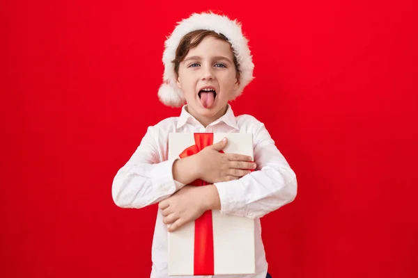 Malý Kavkazský Chlapec Nosí Vánoční Klobouk Drží Dárky Vyčnívající Jazyk — Stock fotografie