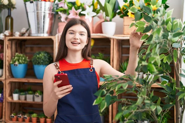 年轻的高加索女人花匠用智能手机对花匠充满自信地微笑 — 图库照片