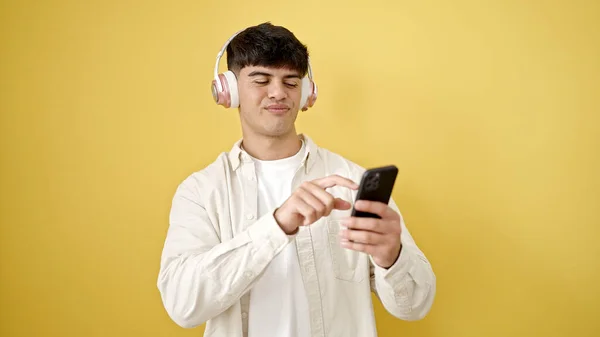 用智能手机在孤立的黄色背景上戴耳机的年轻人 — 图库照片