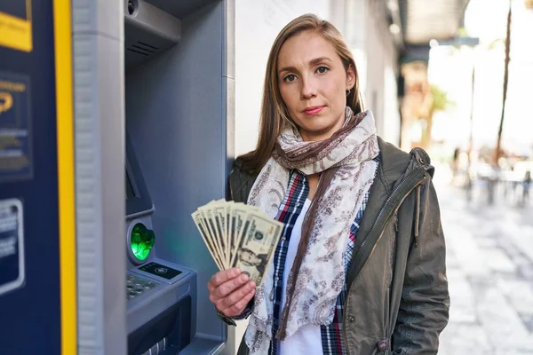 Young Blonde Woman Holding Dollars Banknotes Atm Machine Thinking Attitude — Stock Photo, Image