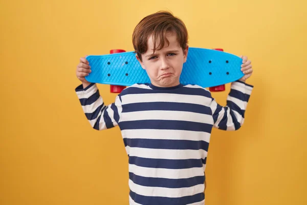 黄色の背景にスケートを保持する小さな白人の少年は落ち込んでおり 苦痛のために心配し 怒って恐れて泣いています 悲しい表情 — ストック写真