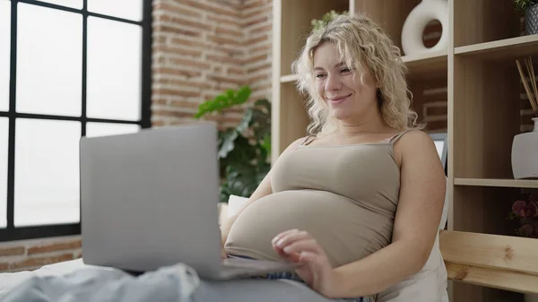年轻的孕妇躺在床上看笔记本电脑上的视频 — 图库照片