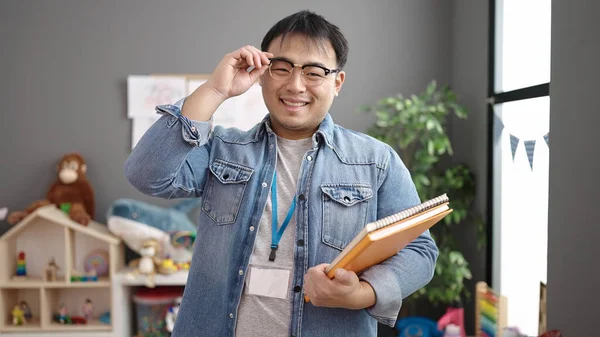Young Chinese Man Teacher Smiling Confident Holding Books Kindergarten — ストック写真