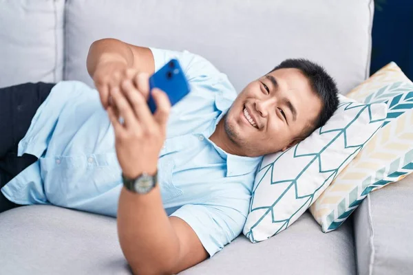 Joven Hombre Chino Usando Teléfono Inteligente Acostado Sofá Casa —  Fotos de Stock