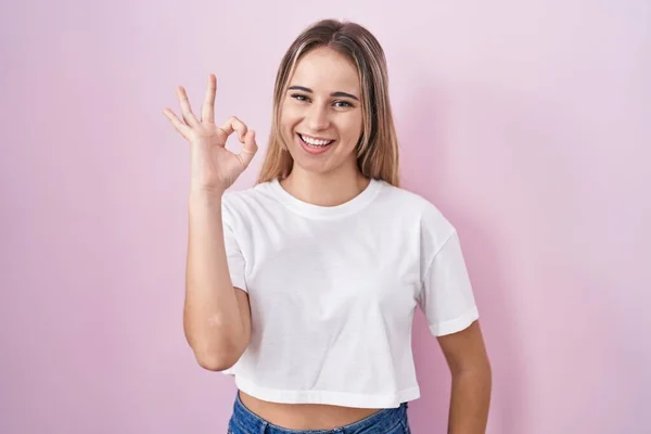 Pembe Arka Planda Duran Genç Sarışın Kadın Gülümsüyor Parmaklarıyla Tamam — Stok fotoğraf