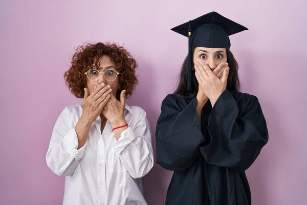 卒業キャップと式用のローブを着たヒスパニック系の母親と娘は間違いのために手で口をカバーショックを受けました 秘密の概念 — ストック写真