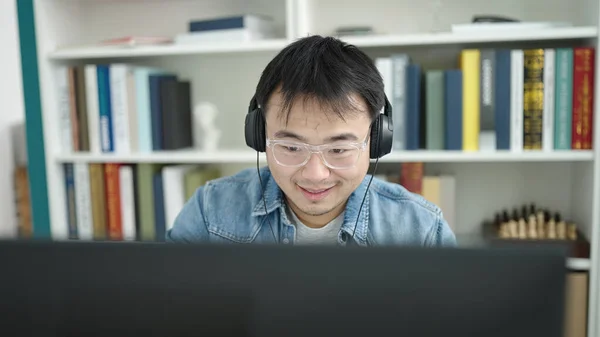 Young chinese man student using computer and headphones at library university