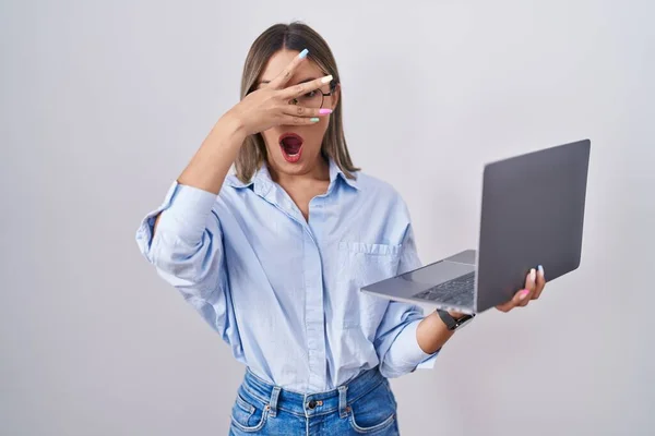 顔と目を手で覆い 恥ずかしい表情の指を通して見て コンピュータのラップトップの目を使用して働いている若い女性 — ストック写真