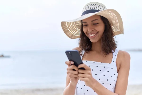 Young African American Woman Wearing Summer Hat Using Smartphone Seaside — Zdjęcie stockowe