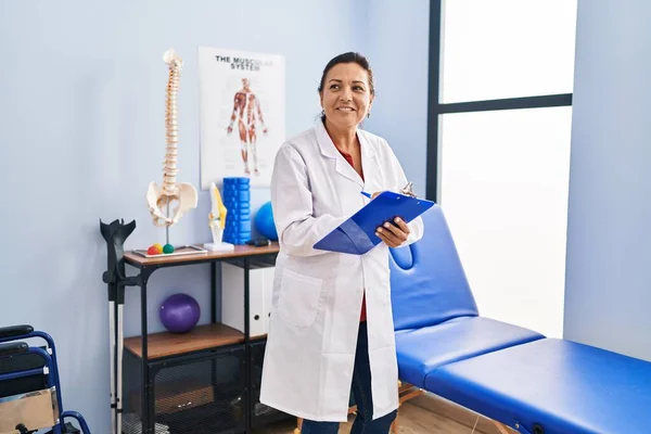 Middle Age Hispanic Woman Physiotherapist Writing Clipboard Rehab Clinic — Stockfoto
