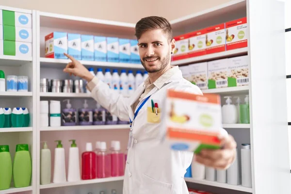 Молодой Кавказский Фармацевт Улыбается Уверенно Держа Витаминный Пакет Аптеке — стоковое фото