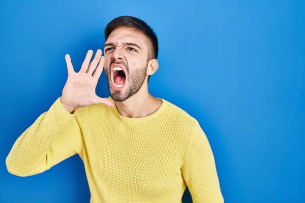 ヒスパニック系の男性の青の背景に叫んで立って大声で口の上に手で横に叫んで コミュニケーションの概念 — ストック写真