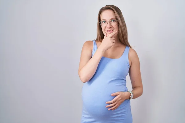 若い妊婦の白い背景の上に手をあごの質問については 集中的な表現を考えて立っている 笑顔で思いやりのある顔 疑わしい概念 — ストック写真