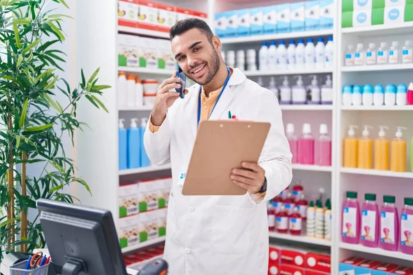 Young Hispanic Man Pharmacist Talking Smartphone Reading Document Pharmacy — Stock fotografie