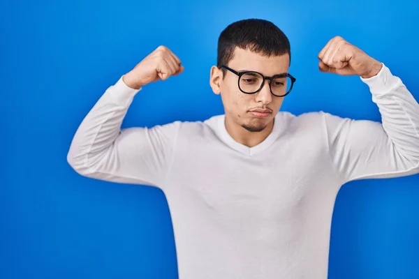 年轻的阿拉伯男子穿着休闲的白色衬衫 戴着眼镜 露出胳膊肌肉 带着自豪的笑容 健身概念 — 图库照片