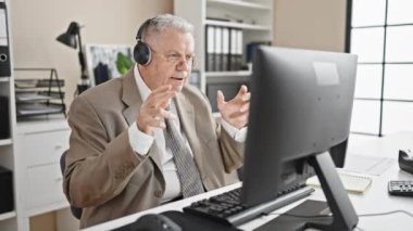 Orta yaşlı, kır saçlı, iş adamı. Ofiste bilgisayar ve kulaklık kullanıyor.