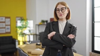 Genç, sarışın, iş kadını, gülümseyen, kendine güvenen, kollarını kavuşturup ofiste el kol kola duran.