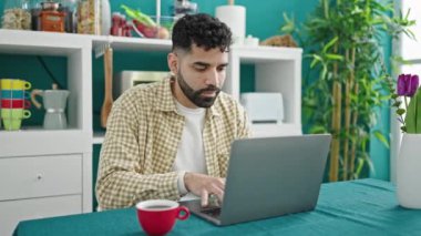 Sofrada dizüstü bilgisayar kullanan İspanyol genç yemek odasında kazanan ifadesiyle oturuyor.