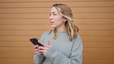 Tecrit edilmiş ahşap arka planda ciddi bir ifadeyle akıllı telefon kullanan genç sarışın kadın.