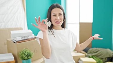 Genç, güzel, İspanyol bir kadın yeni evinde elinde anahtarlarla görüntülü arama yapıyor.