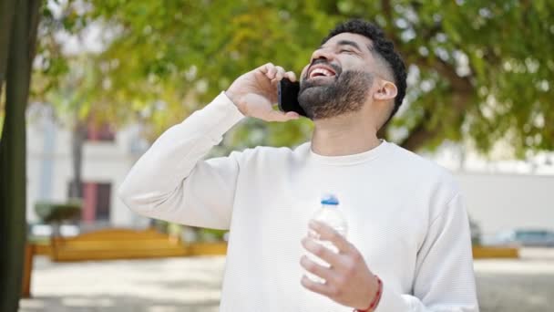 Молодий Іспаномовний Чоловік Тримає Пляшку Води Розмовляючи Смартфоні Парку — стокове відео