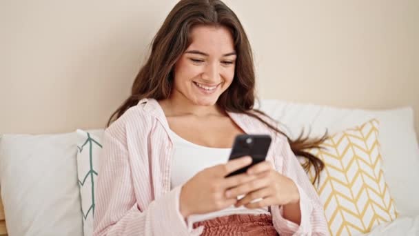 年轻美丽的惊慌失措的女人坐在卧室的床上用智能手机 — 图库视频影像