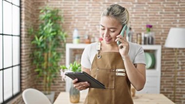 Önlük giymiş genç, güzel bir İspanyol kadın yemek odasında akıllı telefondan konuşuyor.