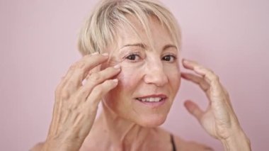 Orta yaşlı sarışın kadın, pembe arka planda kendine güvenen, güler yüzlü bir kadın.