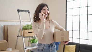 Genç, güzel, İspanyol bir kadın yeni evinde akıllı telefon paketiyle konuşuyor.