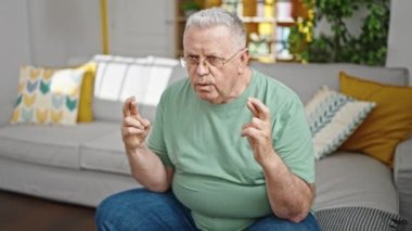 Orta yaşlı, kır saçlı bir adam futbol maçı seyrediyor. Kanepede oturuyor.