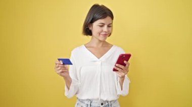 Akıllı telefon ve kredi kartıyla alışveriş yapan genç, güzel İspanyol kadın izole edilmiş sarı arka planda